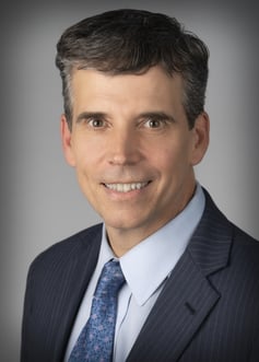 Hastings professional headshot photo. He is in a grey suite with blue patterned tie and white collared shirt.